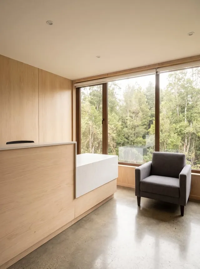 Recepción luminosa de una clínica dental, con sillón de espera, mostrador de madera y eucaliptos al otro lado del ventanal